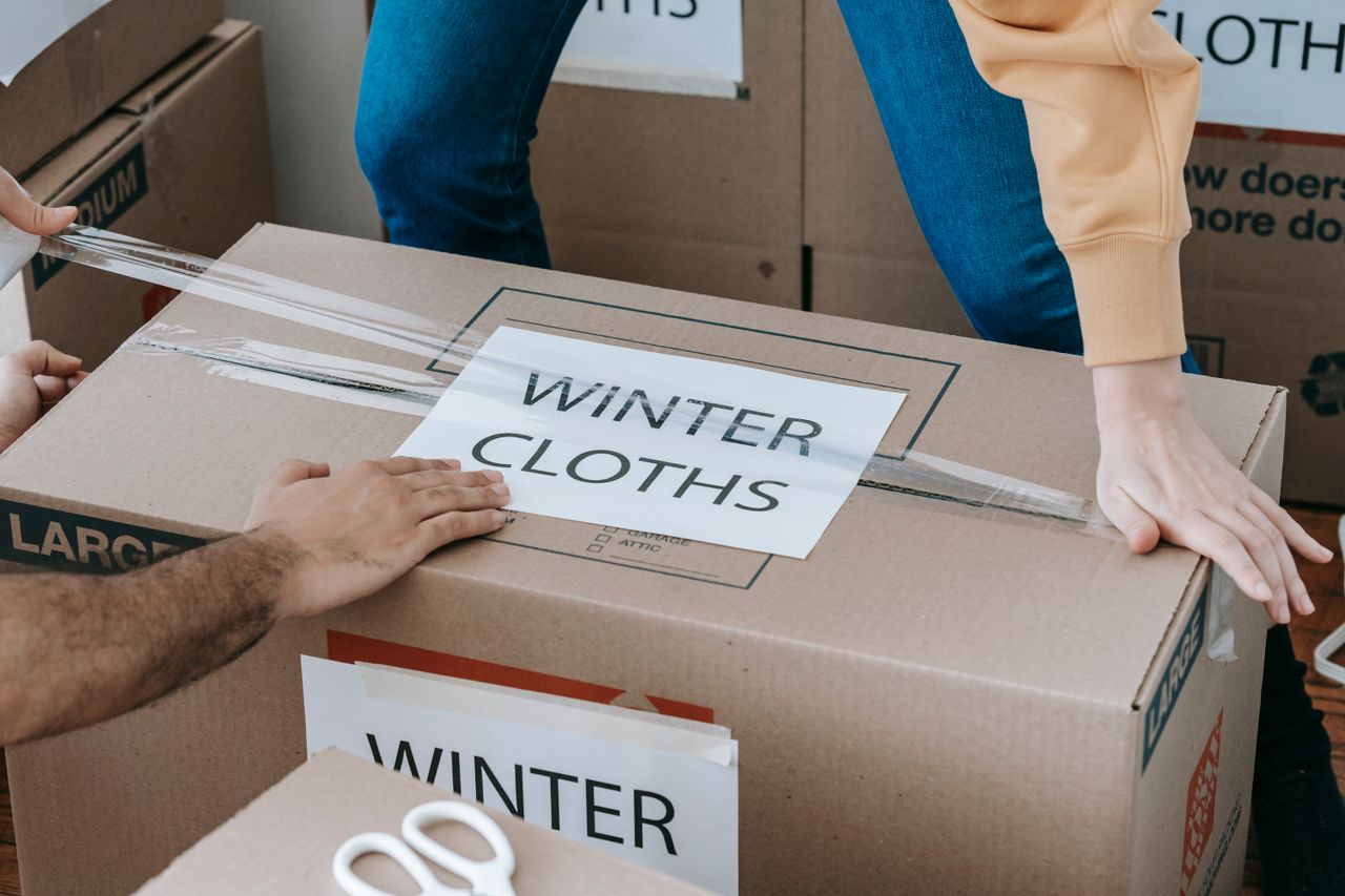 Close-up of hands packing a box labeled Winter Clothes for relocation, emphasizing organized moving.